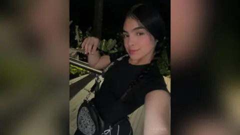 Young woman in a black t-shirt and crossbody bag posing outdoors at night with a moody aesthetic.