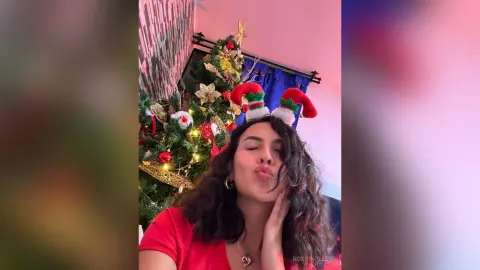 RossiNoleen pouts her lips while wearing red and white elf ears next to a decorated Christmas tree.