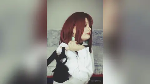 EstherTrix with red hair wearing a white shirt and holding a black high heel shoe.