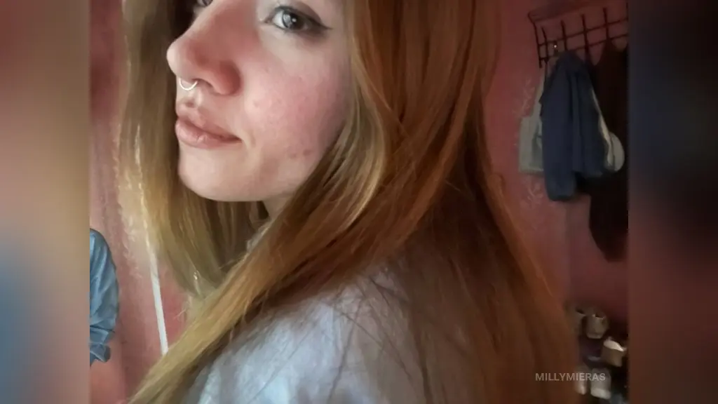 Close-up portrait of a young woman with long brown hair wearing a green tank top in a bright indoor setting.