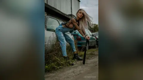 LeslyAnderson stands leaning against a light blue car wearing a black sheer mesh top and light blue denim jeans.