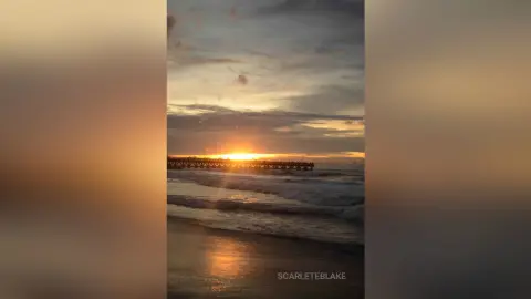 Golden sunset over a wooden pier with waves crashing on a tranquil beach at dusk.