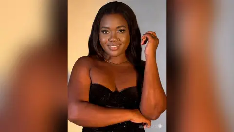 Smiling Black woman in a glamorous black strapless dress posing against a warm studio background.