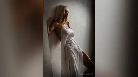 LeslyAnderson poses against a wall wearing a sheer white strapless dress that clings to her body.