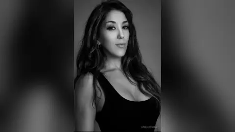 Elegant woman with long wavy hair wearing a black tank top in a moody black and white studio portrait.