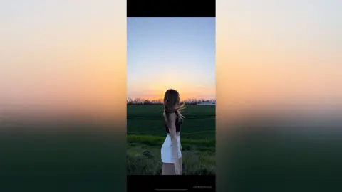 Young woman in a black top and white shorts standing in a green field during a golden sunset.
