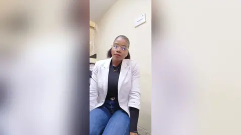 Confident Black woman in a white blazer and black top sitting in a bright modern office setting.