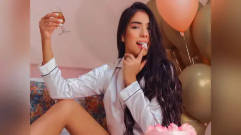 Young woman in white silk pajamas eating cake near peach balloons in a celebratory mood.
