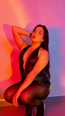 Young woman in a black leather outfit posing against a warm red and blue studio background.