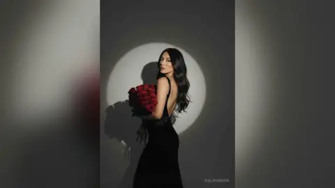 Elegant woman in a black backless dress holding red roses in a moody, dramatic studio setting.
