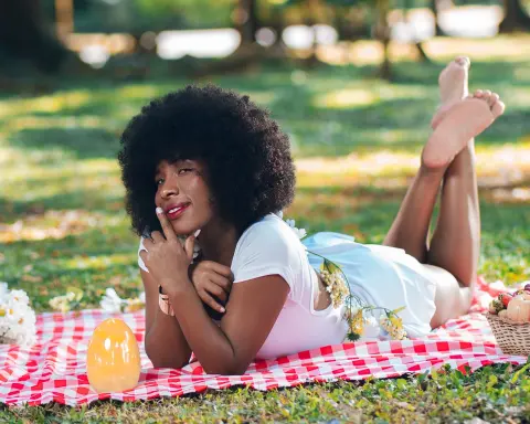 Smiling woman in white outfit lying on a picnic blanket in a sunny park during a relaxing spring day.
