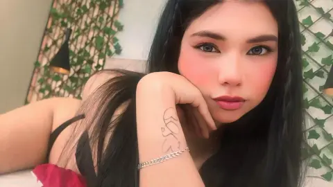 Nathy_Pelaez rests her chin on her hand, looking at the camera with long black hair and red lipstick.