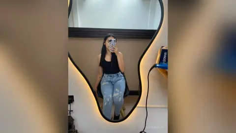 ZoeMonrow poses in a mirror wearing a black tank top and light blue ripped jeans, holding her phone to take a mirror selfie.
