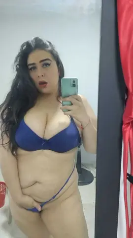 Curvy woman in a blue bikini posing for a mirror selfie in a bright indoor setting.