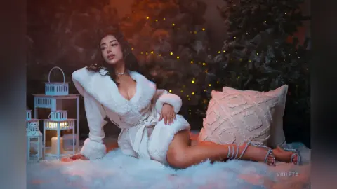 Beautiful woman in a white fuzzy robe relaxing on a snowy rug near lanterns in a cozy winter setting.