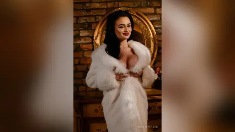 Elegant woman in a luxurious white faux fur coat posing in a warm, rustic brick interior.