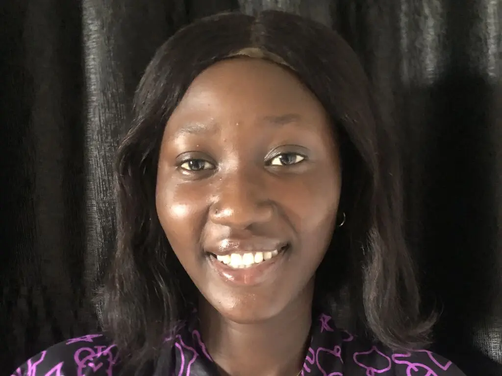 Smiling Black woman in a purple patterned blouse posing against a dark curtain background.