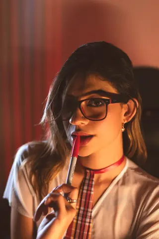 Young woman in glasses and white top holding a red marker in warm, moody indoor lighting.