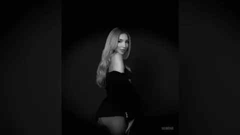 Elegant woman in a black dress posing against a dark background for a moody, sophisticated portrait.