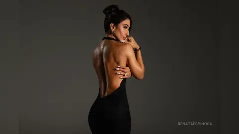 Elegant woman in a backless black evening gown posing gracefully against a dark studio background.