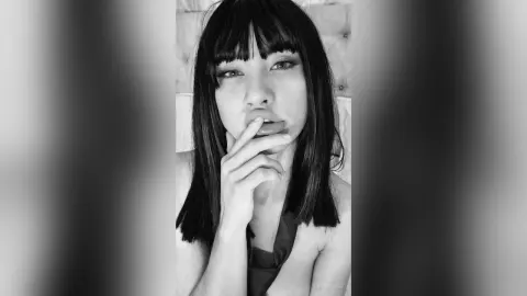 Moody black and white portrait of a young woman with bangs looking thoughtfully into the camera.