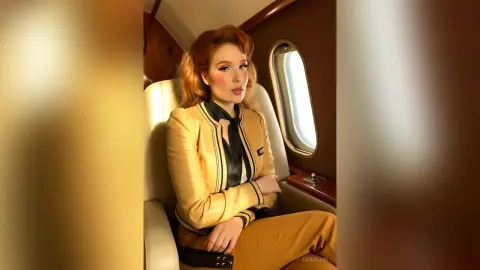 Elegant woman in a gold blazer sitting in a luxury private jet interior with a sophisticated mood.