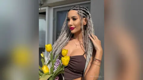 Beautiful woman with long silver braids holding yellow tulips in a bright outdoor setting.