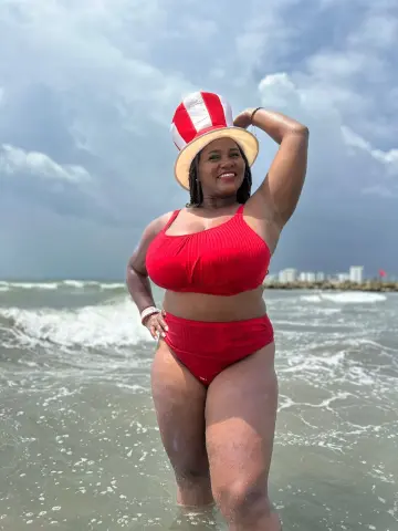 Smiling woman in a red bikini and straw hat enjoying a sunny day at the beach waves.