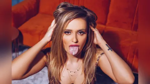 Gia runs her hands through her long blonde hair while sticking out her tongue in a close-up shot.