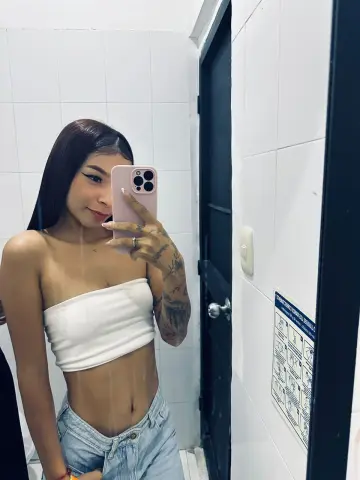 Young woman in a white tube top and denim jeans taking a mirror selfie in a modern bathroom.
