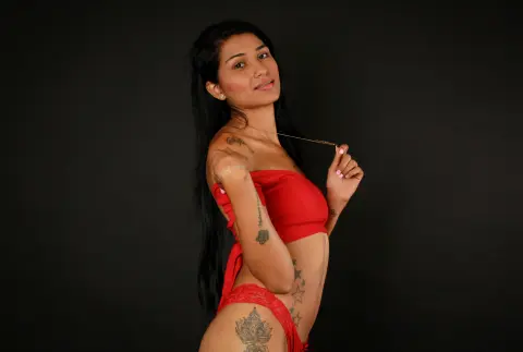 Tattooed woman in a red strapless top posing confidently against a black background.