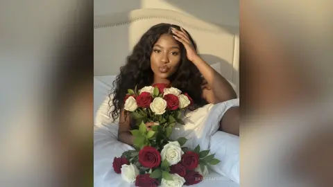 Beautiful Black woman in a romantic setting holding a large bouquet of red and white roses on a white bed.