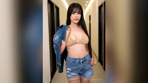 Young woman in a beige crop top and denim shorts posing confidently in a modern hallway.