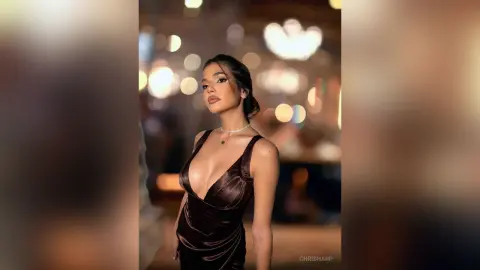 Elegant woman in a plunging dark brown velvet dress posing in a warm, dimly lit upscale restaurant setting.