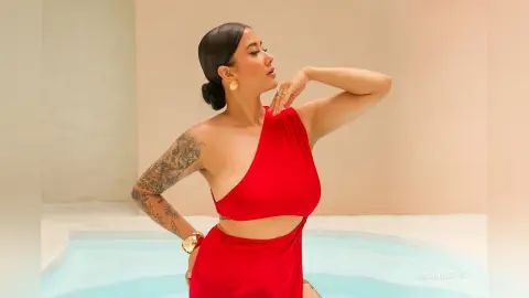 JuliahLewis poses in a red halter-neck top and matching skirt, showing off her arm tattoos and slicked-back hair by a pool.