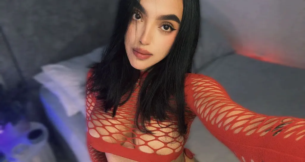 Young woman with glam makeup wearing a red halter top in a soft indoor setting.