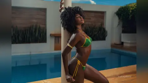 Serene Black woman in a green crochet bikini leaning against a pillar by a luxury poolside setting.