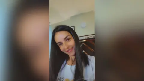 Smiling young woman with long dark hair wearing a white t-shirt in a bright indoor setting.
