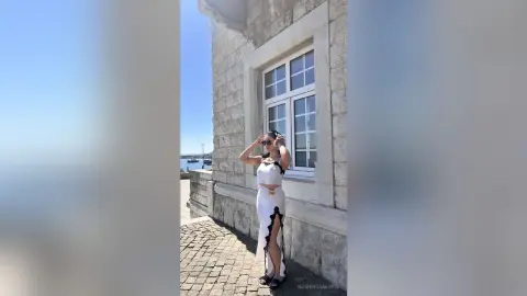 Stylish woman in a white crop top and slit skirt posing by a stone building on a sunny day.