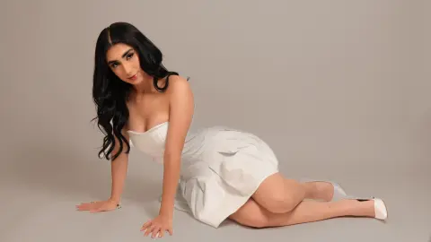 Elegant woman in a white strapless cocktail dress sitting on a neutral background with a sophisticated mood.