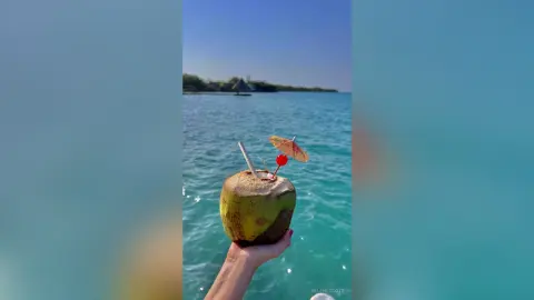 Refreshing coconut drink with a straw held against a sunny tropical ocean backdrop for a summer vacation mood.