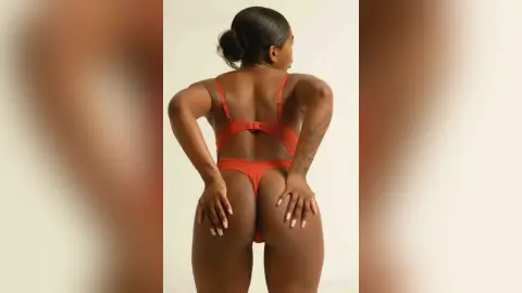 Back view of a woman in a red one-piece swimsuit posing against a neutral studio background.
