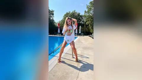 Stylish woman in a white cutout tunic and gold strappy sandals relaxing by a sunny outdoor swimming pool.