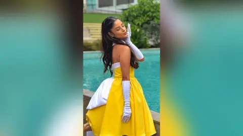 TefyRusso poses in a bright yellow strapless dress and long white gloves, standing by a blue swimming pool with her hair down.