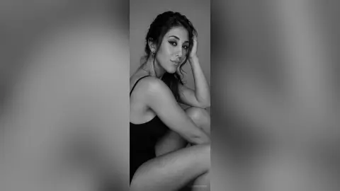 Elegant woman in a black bodysuit posing with a moody, contemplative expression in a minimalist studio setting.