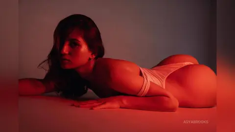 Young woman in white lingerie lying on a floor under moody red lighting for a sensual portrait.