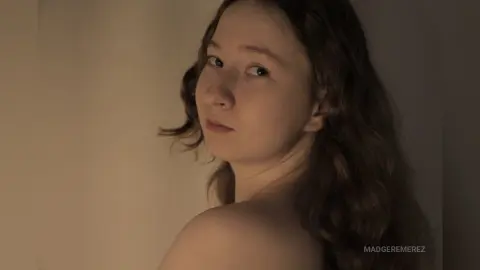 Young woman with long wavy hair posing in soft, moody indoor lighting for a dreamy portrait.