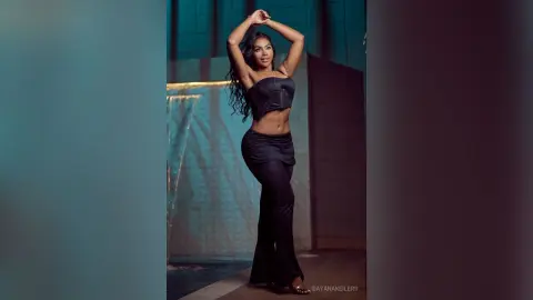 DayanaKeilers poses with her hands behind her head, wearing a black strapless bustier and matching black pants.