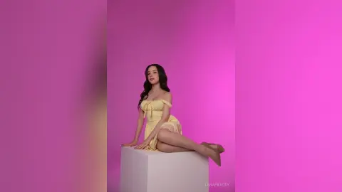 Elegant woman in a yellow sundress sitting on a white pedestal against a vibrant pink background.