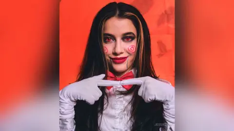 JessieLiu wears a white shirt and red bow tie with red makeup and white gloves against a red background.